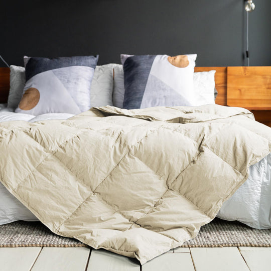 A natural cotton down throw blanket on a bed with a dark wall and wood headboard