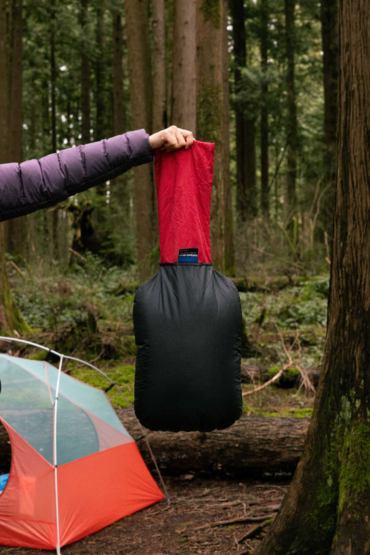 Person holding a Geoduck Pillow with its internal stuff sack pulled out while in a green, mossy forest