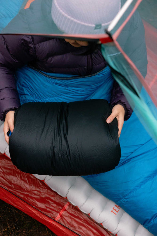 Person inside a tent holding a black Geoduck Down Pillow