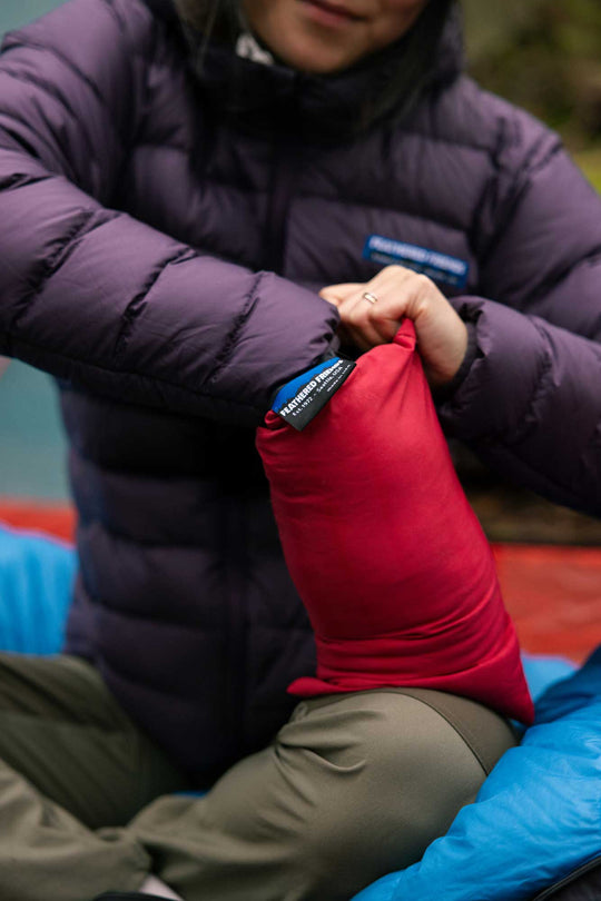 A person in a purple jacket stuffing a Geoduck Pillow into its integrated stuff sack