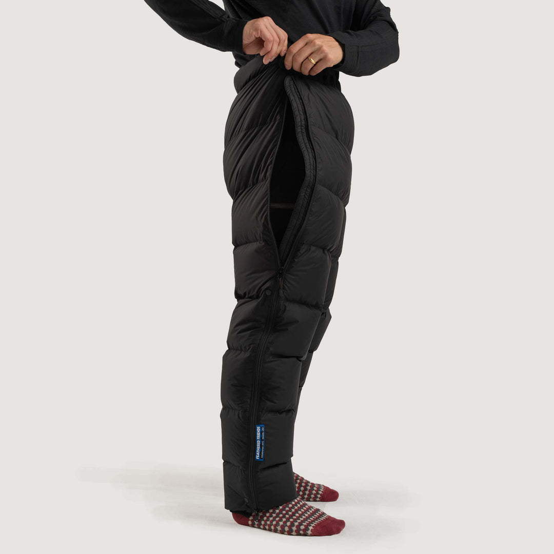 Studio side view zipper detail of a man wearing a black Feathered Friends Helios down pants