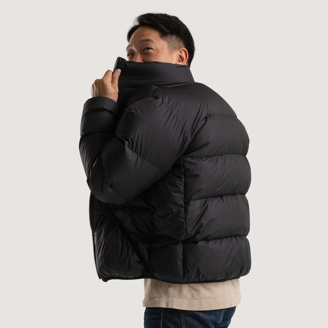 Studio side view of a man wearing a black Feathered Friends Helios jacket
