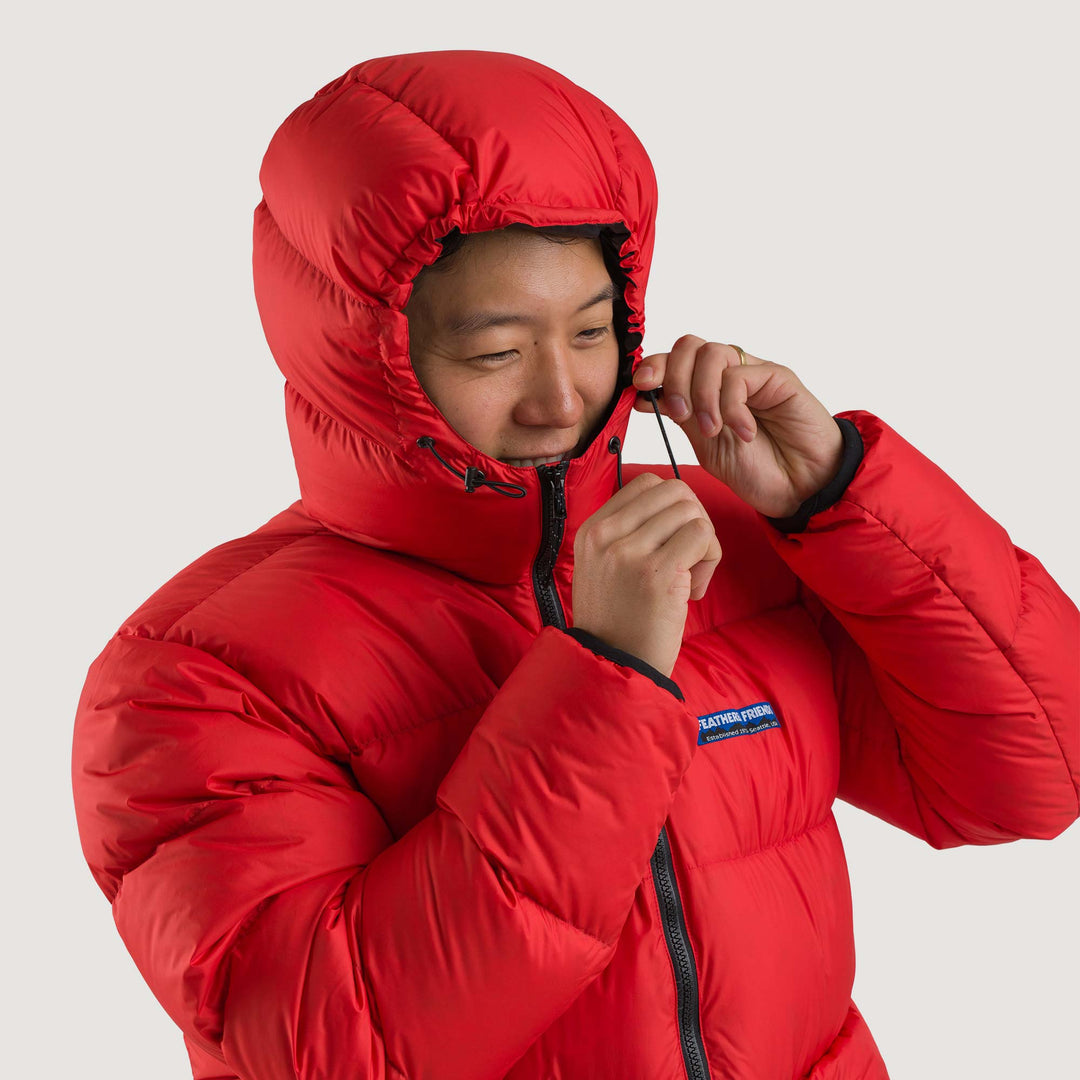Studio front view hood detail of a man wearing a poppy red Feathered Friends Hooded Helios down puffer jacket