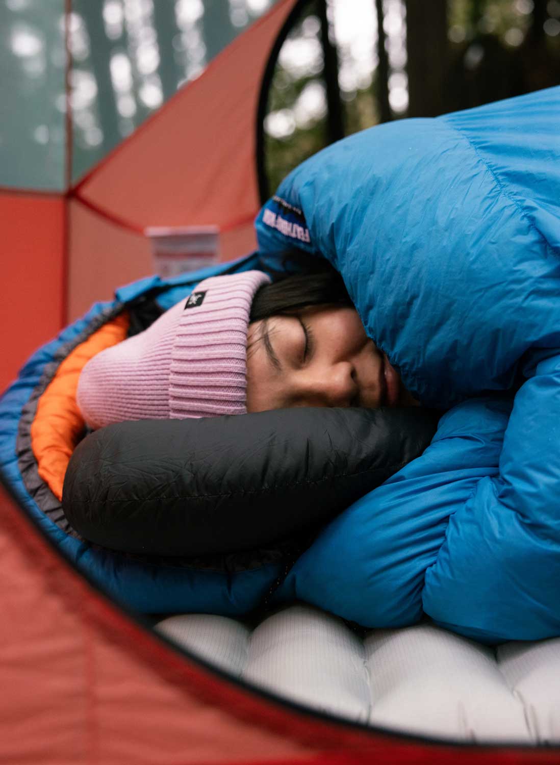 Person sleeping in a ultralight cerulean blue sleeping bag in a red tent