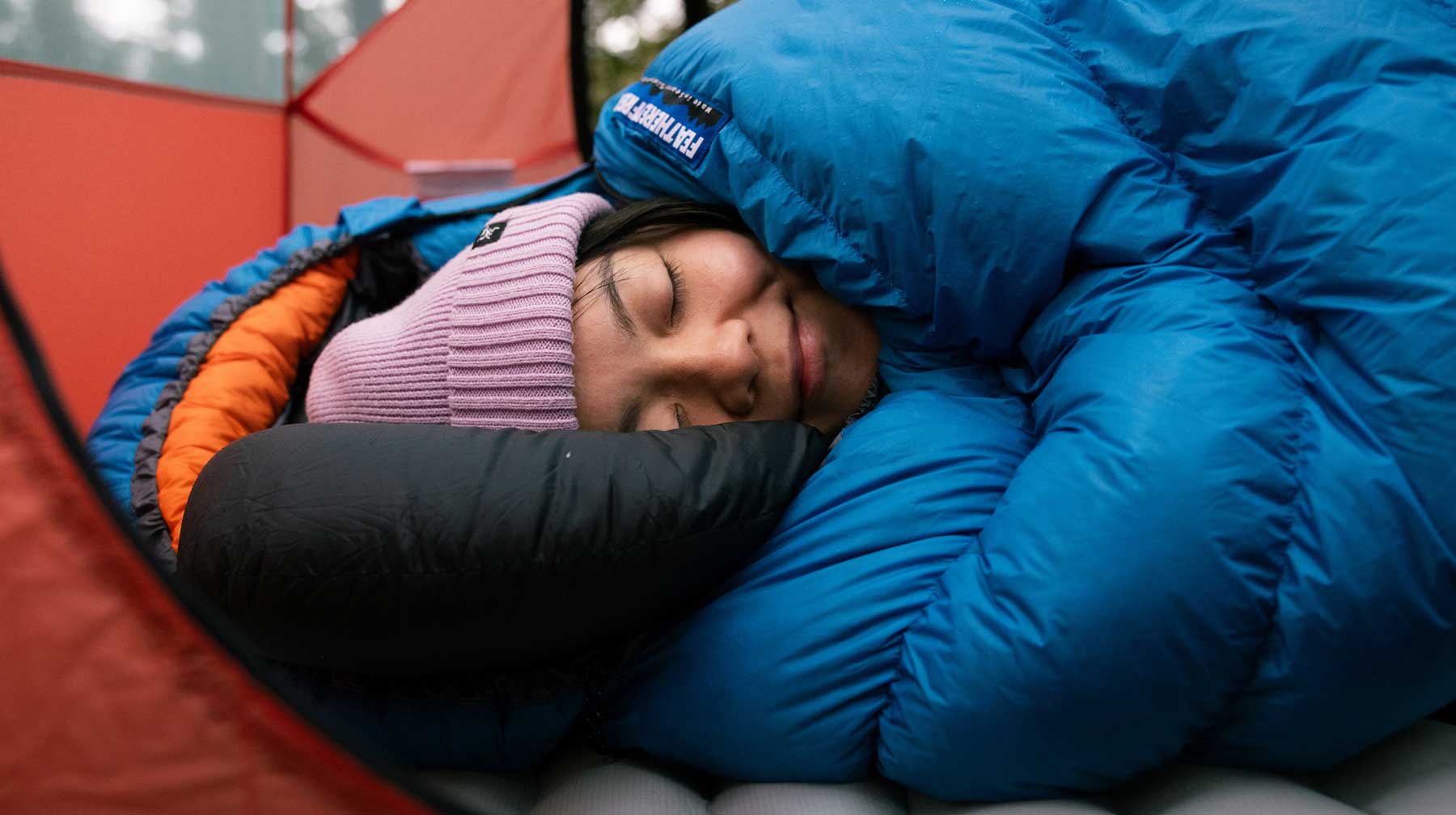 Person sleeping in a ultralight cerulean blue sleeping bag in a red tent
