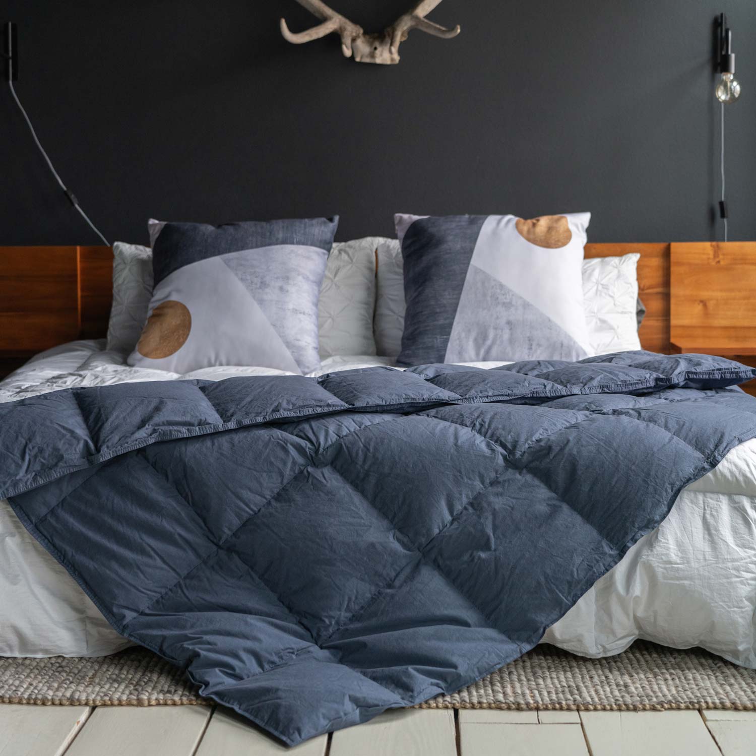 Feathered Friends organic down throw Navy blue color on a bed with wood headboard, large pillows, and antlers on the wall