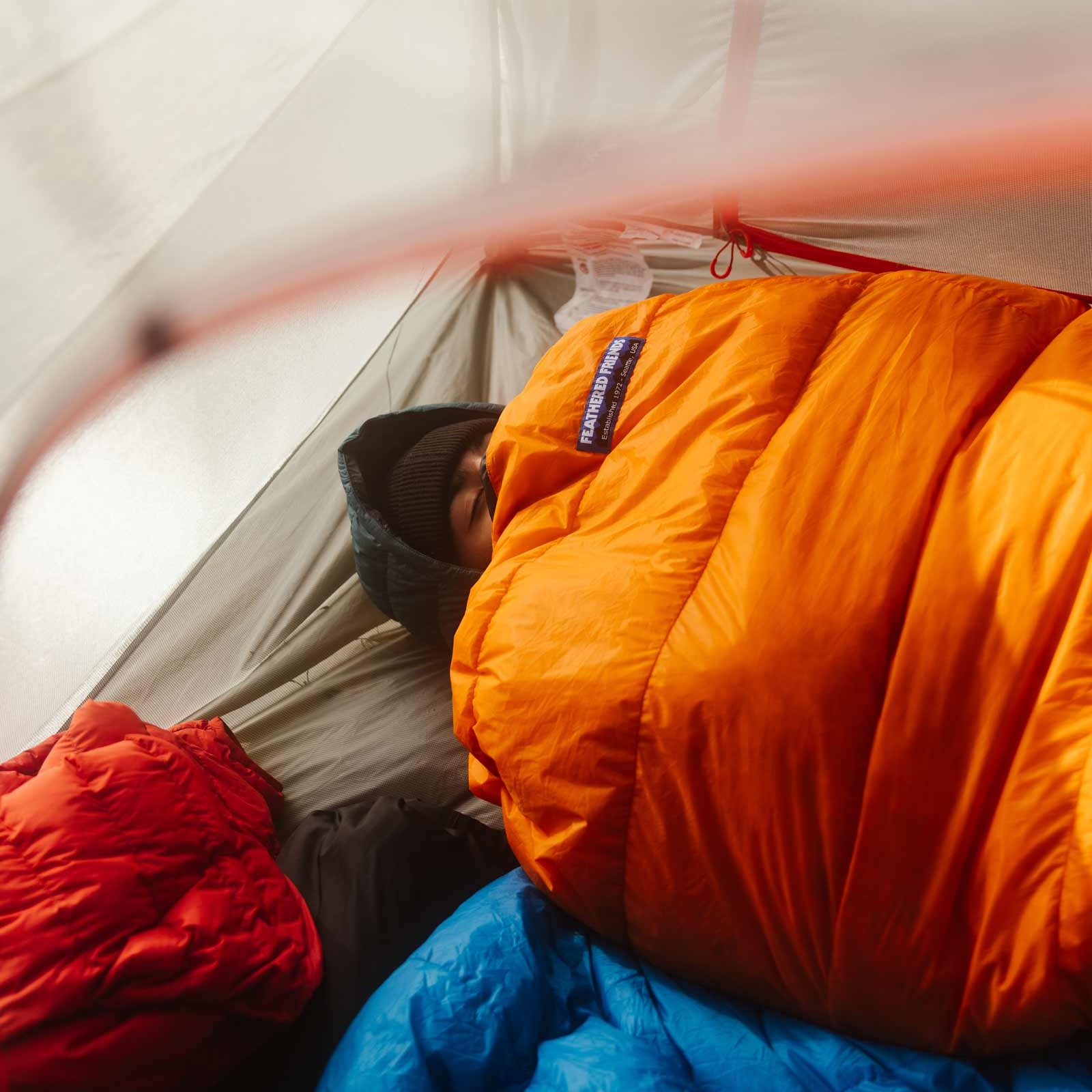 Person sleeping in a Flame orange Feathered Friends Vireo ultralight sleeping bag inside a tent