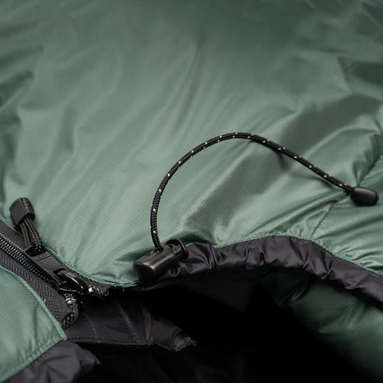 Close-up of a green sleeping bag with zipper and cord, focusing on texture and details.
