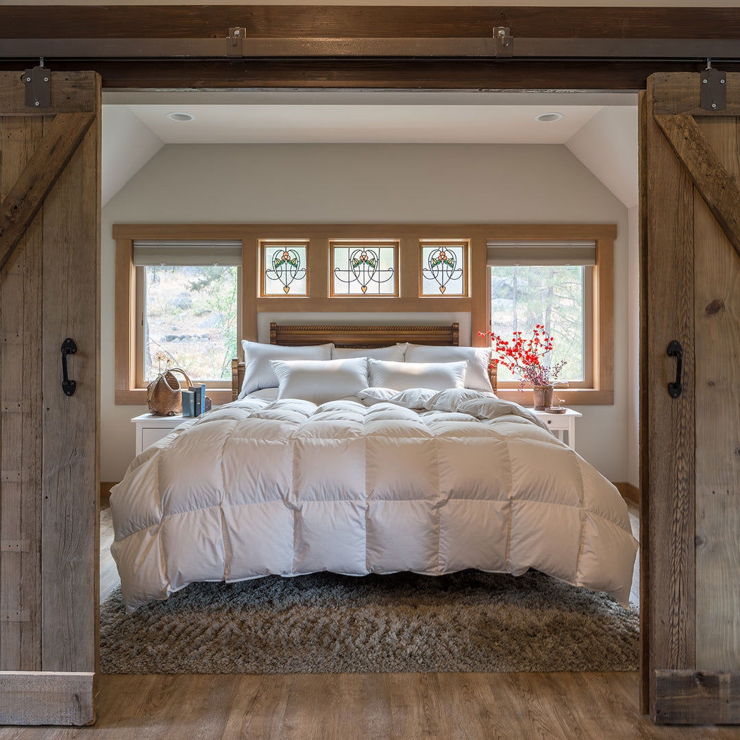 The Feathered Friends Baffled Box Down Comforter on a bed framed by sliding barn doors