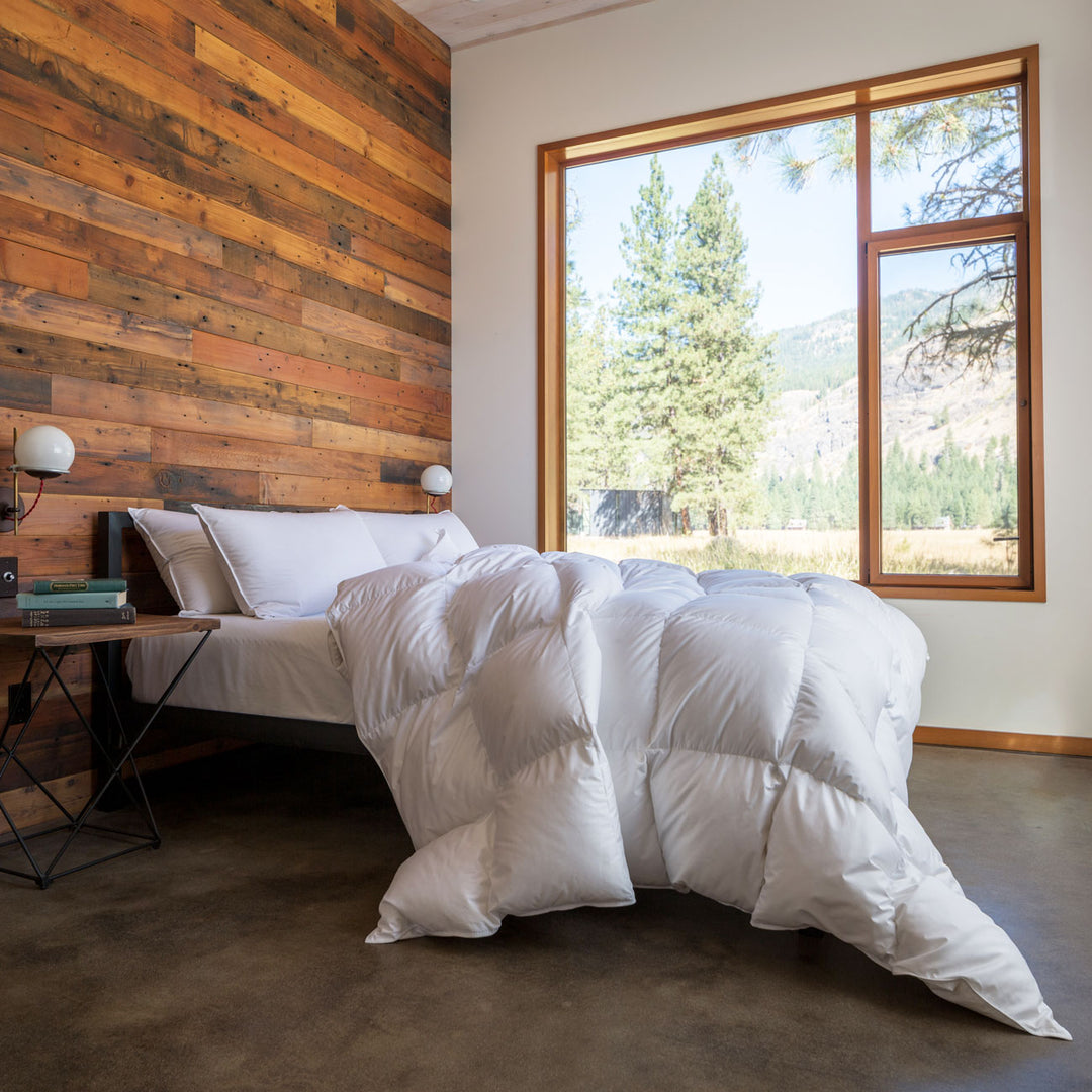 The Feathered Friends Bavarian 700 Down Comforter cascading off a bed in a bedroom in the forest of the Methow Valley